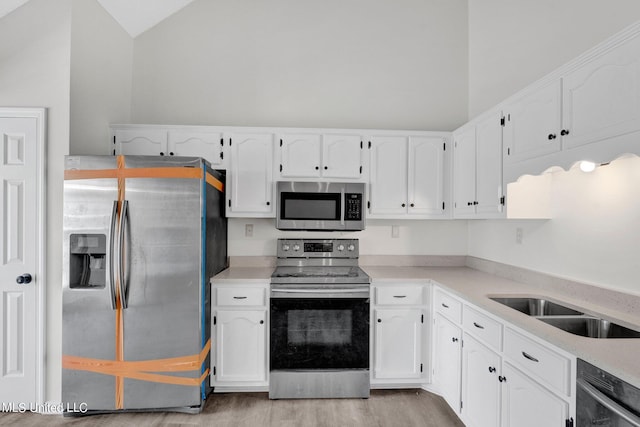 kitchen featuring lofted ceiling, appliances with stainless steel finishes, light hardwood / wood-style flooring, and white cabinetry