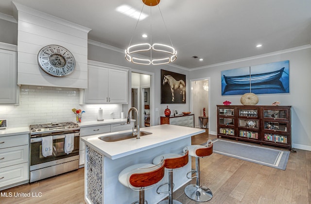 kitchen with an island with sink, sink, stainless steel range with gas stovetop, and white cabinets