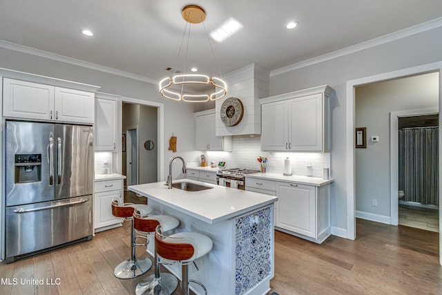 kitchen with sink, white cabinetry, hanging light fixtures, appliances with stainless steel finishes, and an island with sink