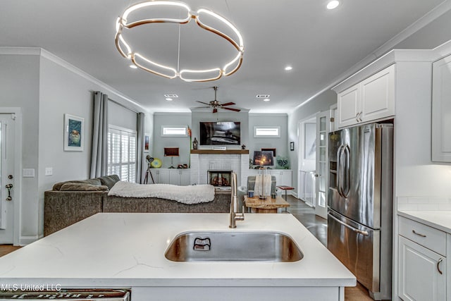 kitchen with an island with sink, sink, stainless steel fridge, and light stone counters