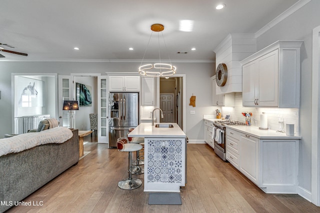 kitchen featuring pendant lighting, tasteful backsplash, white cabinets, stainless steel appliances, and a center island with sink