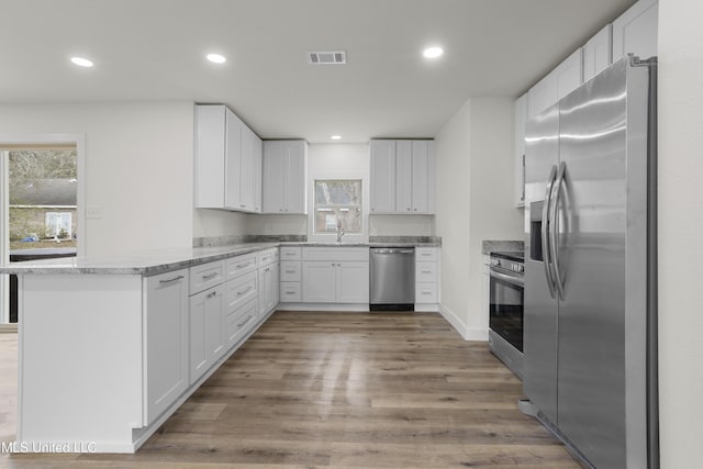 kitchen with sink, appliances with stainless steel finishes, white cabinets, kitchen peninsula, and light wood-type flooring