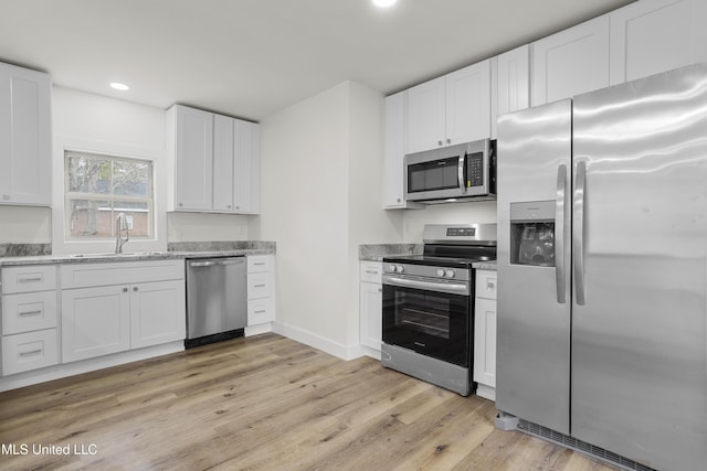 kitchen featuring sink, appliances with stainless steel finishes, white cabinetry, light stone counters, and light hardwood / wood-style floors