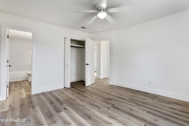 unfurnished bedroom featuring ceiling fan, ensuite bath, light wood-type flooring, and a closet