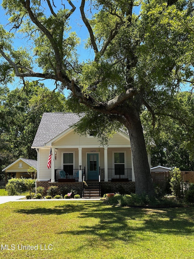 view of front of home featuring a shingled roof, covered porch, and a front lawn