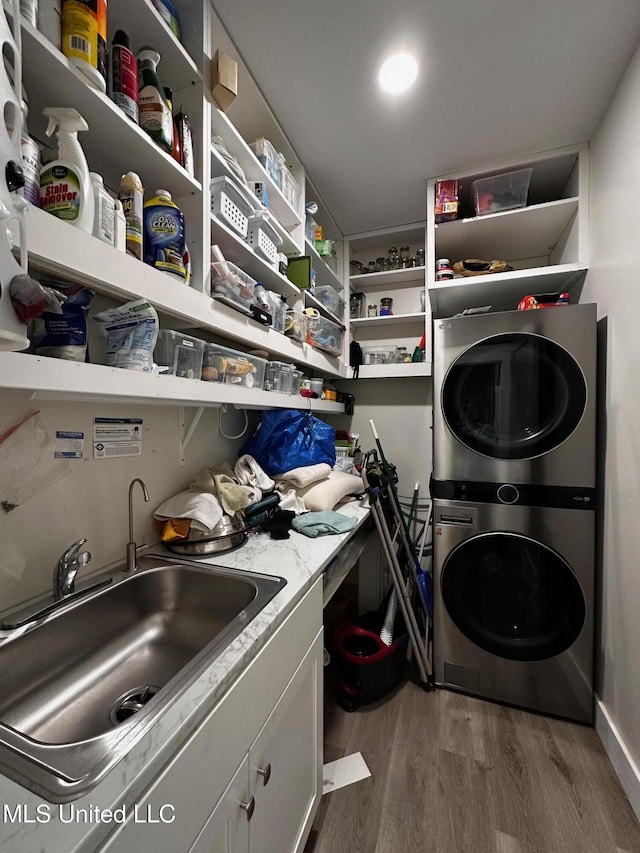 clothes washing area with stacked washing maching and dryer, a sink, wood finished floors, and cabinet space