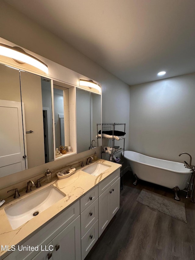 bathroom featuring wood finished floors, double vanity, a sink, and a freestanding tub