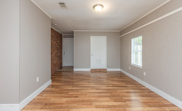 unfurnished room with light wood-type flooring, crown molding, and brick wall