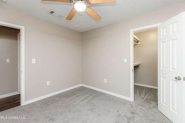 unfurnished bedroom with ceiling fan, a spacious closet, light carpet, and a closet