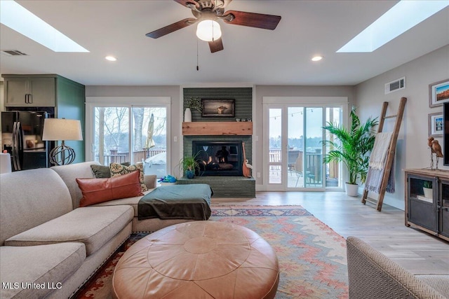 living room with a brick fireplace, light wood-type flooring, and a skylight