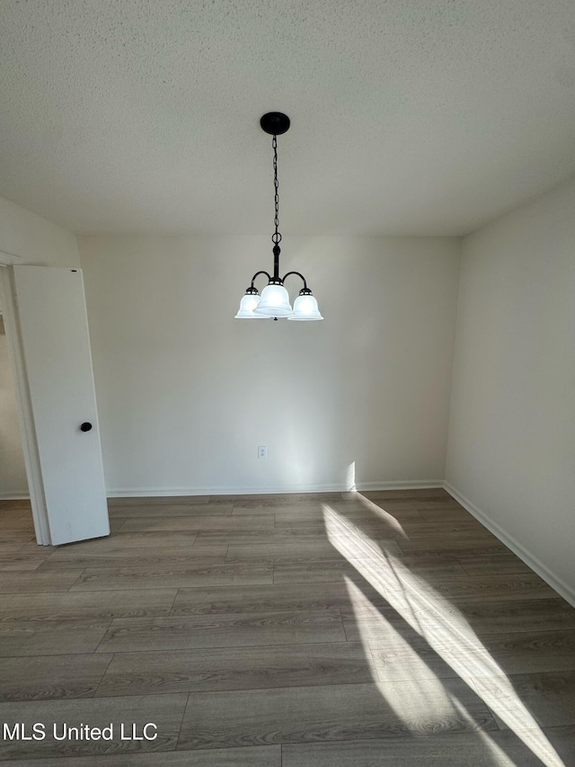 spare room with a chandelier, hardwood / wood-style floors, and a textured ceiling