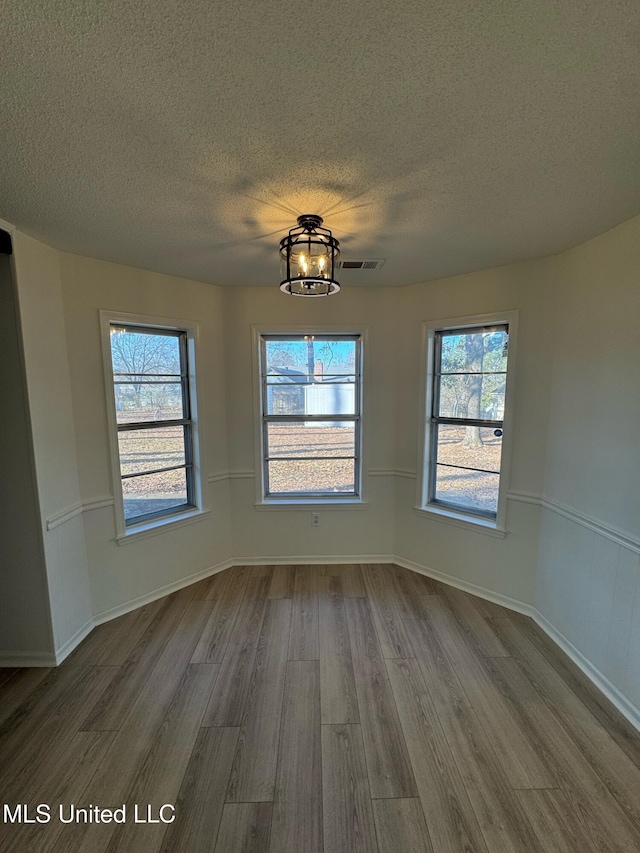 unfurnished dining area featuring an inviting chandelier, hardwood / wood-style flooring, and a textured ceiling