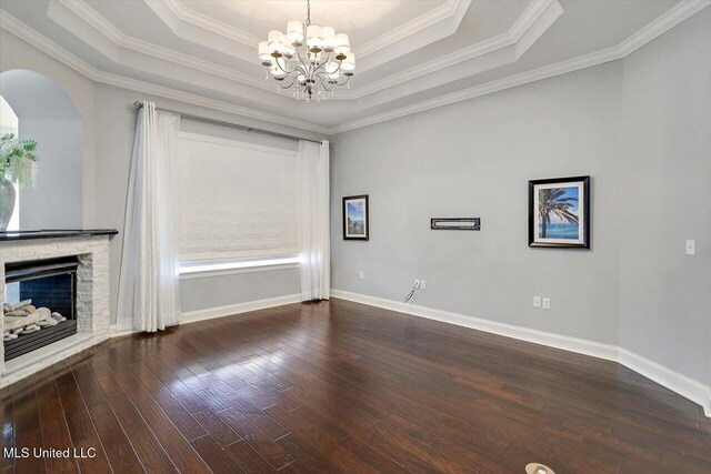 empty room featuring a raised ceiling, crown molding, a chandelier, dark hardwood / wood-style floors, and a stone fireplace