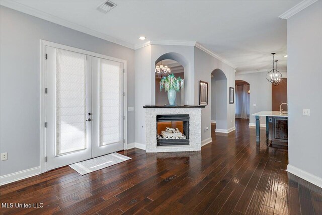 unfurnished living room with french doors, an inviting chandelier, a stone fireplace, dark hardwood / wood-style flooring, and crown molding