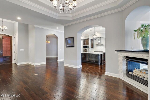 unfurnished living room featuring a fireplace, dark wood-type flooring, a tray ceiling, and ornamental molding