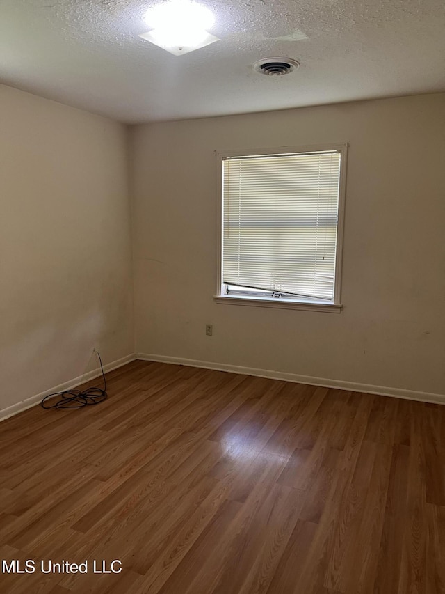 unfurnished room with baseboards, a textured ceiling, wood finished floors, and visible vents