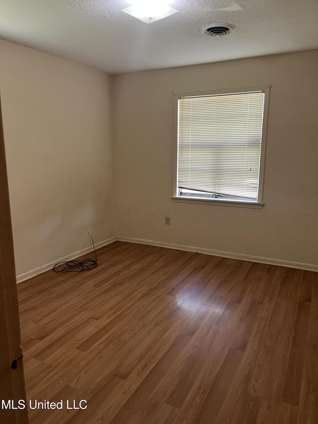 unfurnished room featuring baseboards, visible vents, and wood finished floors