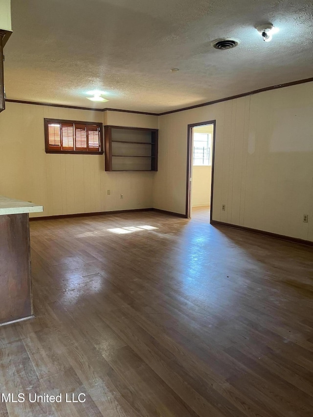 empty room with baseboards, a textured ceiling, wood finished floors, and visible vents