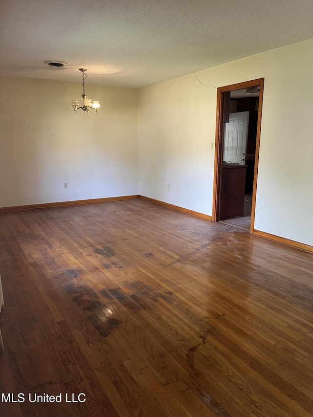 spare room with baseboards, a chandelier, dark wood-style floors, and visible vents