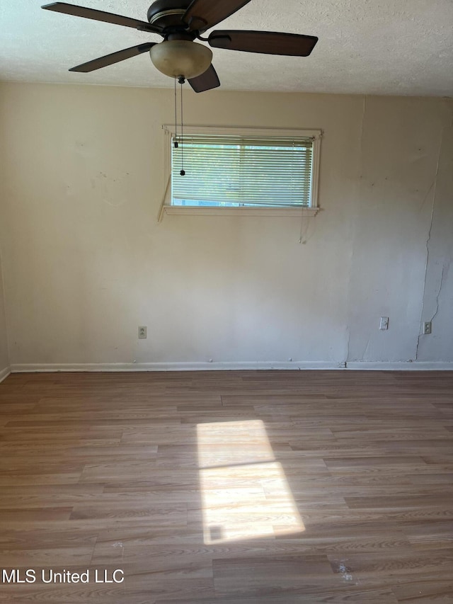 empty room with baseboards, ceiling fan, a textured ceiling, and wood finished floors