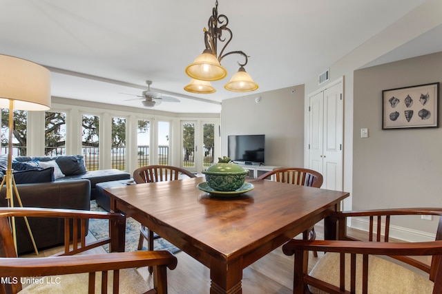 dining space with ceiling fan with notable chandelier and light wood-type flooring