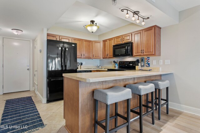 kitchen featuring black appliances, kitchen peninsula, and light tile patterned floors