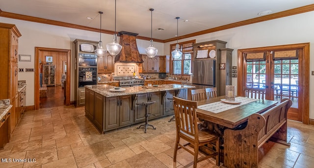 kitchen with stainless steel appliances, light stone counters, a center island, custom range hood, and decorative light fixtures