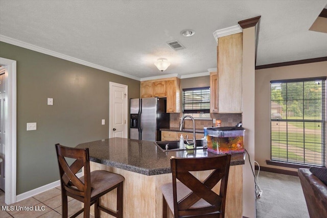 kitchen with stainless steel fridge with ice dispenser, a sink, light brown cabinets, dark countertops, and a peninsula