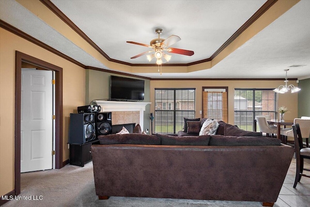 living area featuring ornamental molding, a tray ceiling, a tile fireplace, baseboards, and ceiling fan