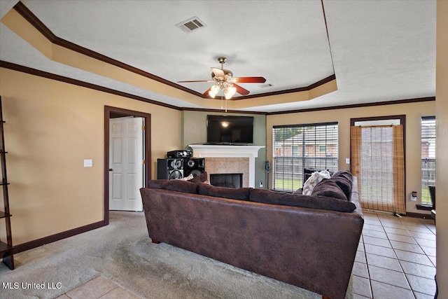living area with a raised ceiling, crown molding, baseboards, a fireplace, and ceiling fan