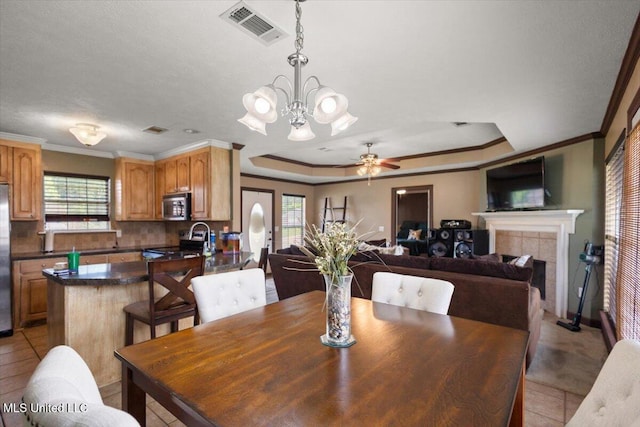 dining area featuring light tile patterned flooring, ceiling fan, a tiled fireplace, crown molding, and a chandelier