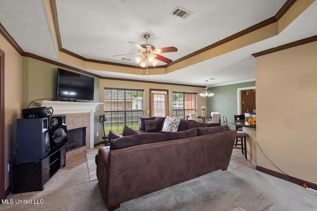 carpeted living room with crown molding, a ceiling fan, a fireplace, a tray ceiling, and baseboards