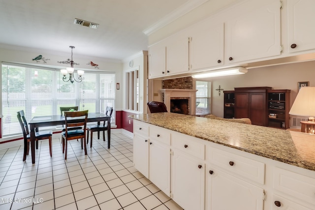 1 Partridge Pl, Long Beach, MS 39560 - kitchen with a brick fireplace, light tile patterned floors, a chandelier, crown molding, and white cabinetry