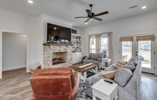 living room with a brick fireplace, crown molding, light hardwood / wood-style flooring, and a healthy amount of sunlight