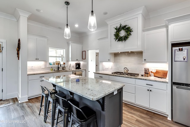 kitchen with a breakfast bar area, white cabinets, hanging light fixtures, ornamental molding, and a center island