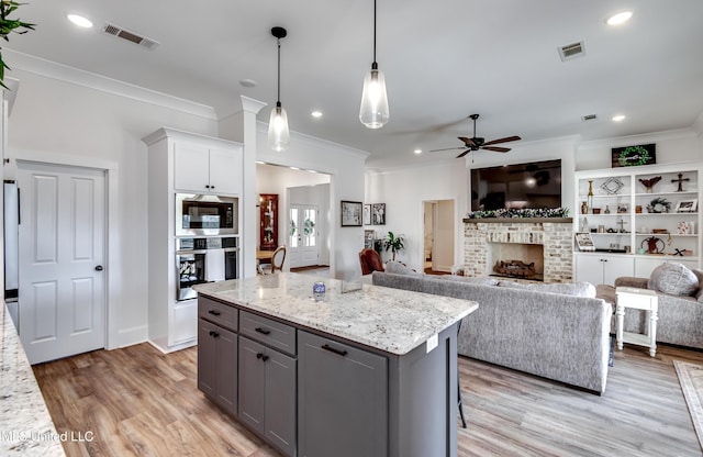 kitchen with gray cabinets, a kitchen island, oven, hanging light fixtures, and light stone countertops