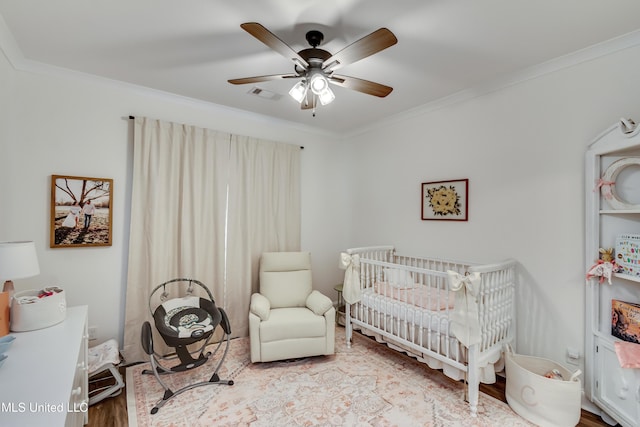 bedroom with ornamental molding, a nursery area, ceiling fan, and light hardwood / wood-style flooring