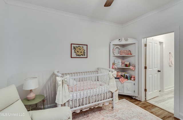 bedroom with a nursery area, ceiling fan, ornamental molding, and hardwood / wood-style floors