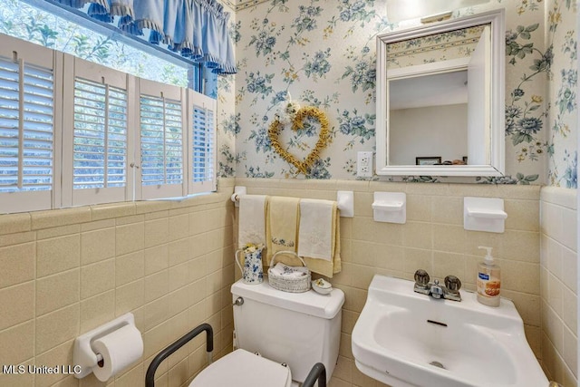 bathroom with toilet, tile walls, plenty of natural light, and sink