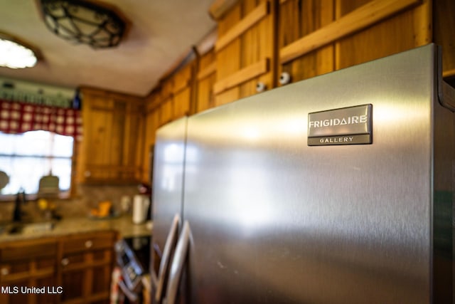 kitchen with a sink, stove, brown cabinetry, and freestanding refrigerator