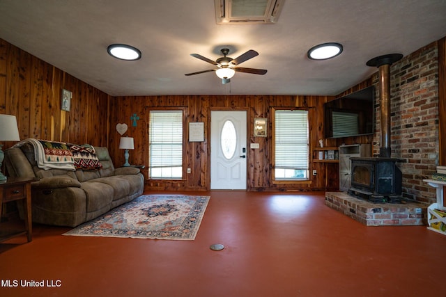 living area featuring wooden walls, visible vents, finished concrete flooring, a wood stove, and a ceiling fan