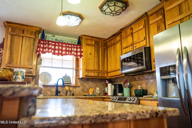 kitchen with light stone counters, a sink, tasteful backsplash, appliances with stainless steel finishes, and brown cabinetry