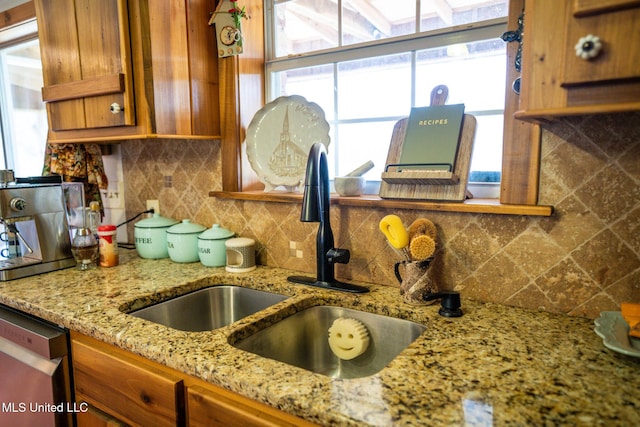 kitchen with a sink, brown cabinetry, decorative backsplash, light stone countertops, and dishwasher