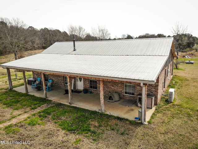 back of house featuring a lawn, a patio area, brick siding, and metal roof