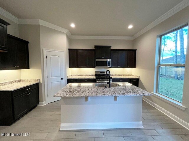 kitchen with light stone counters, ornamental molding, a kitchen island with sink, stainless steel appliances, and a sink