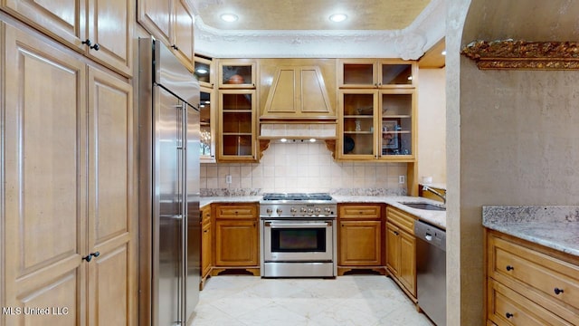 kitchen with sink, light stone counters, premium range hood, backsplash, and high quality appliances