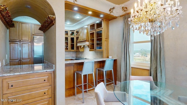 kitchen featuring pendant lighting, built in refrigerator, light stone countertops, tasteful backsplash, and a notable chandelier