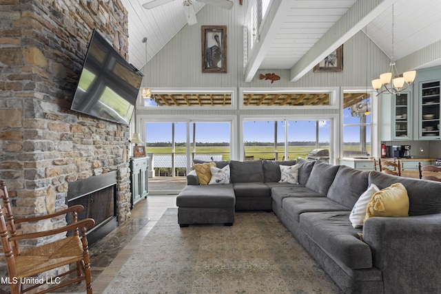 living area with a stone fireplace, wood finished floors, high vaulted ceiling, and ceiling fan with notable chandelier