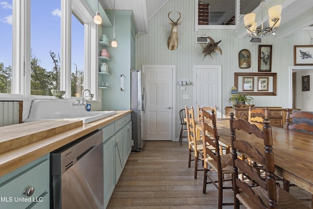 kitchen with light wood finished floors, hanging light fixtures, a sink, butcher block countertops, and appliances with stainless steel finishes