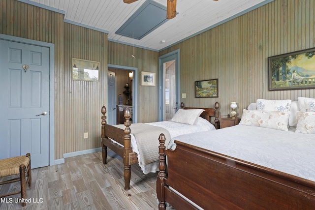 bedroom with a ceiling fan, wood walls, light wood-style flooring, and attic access